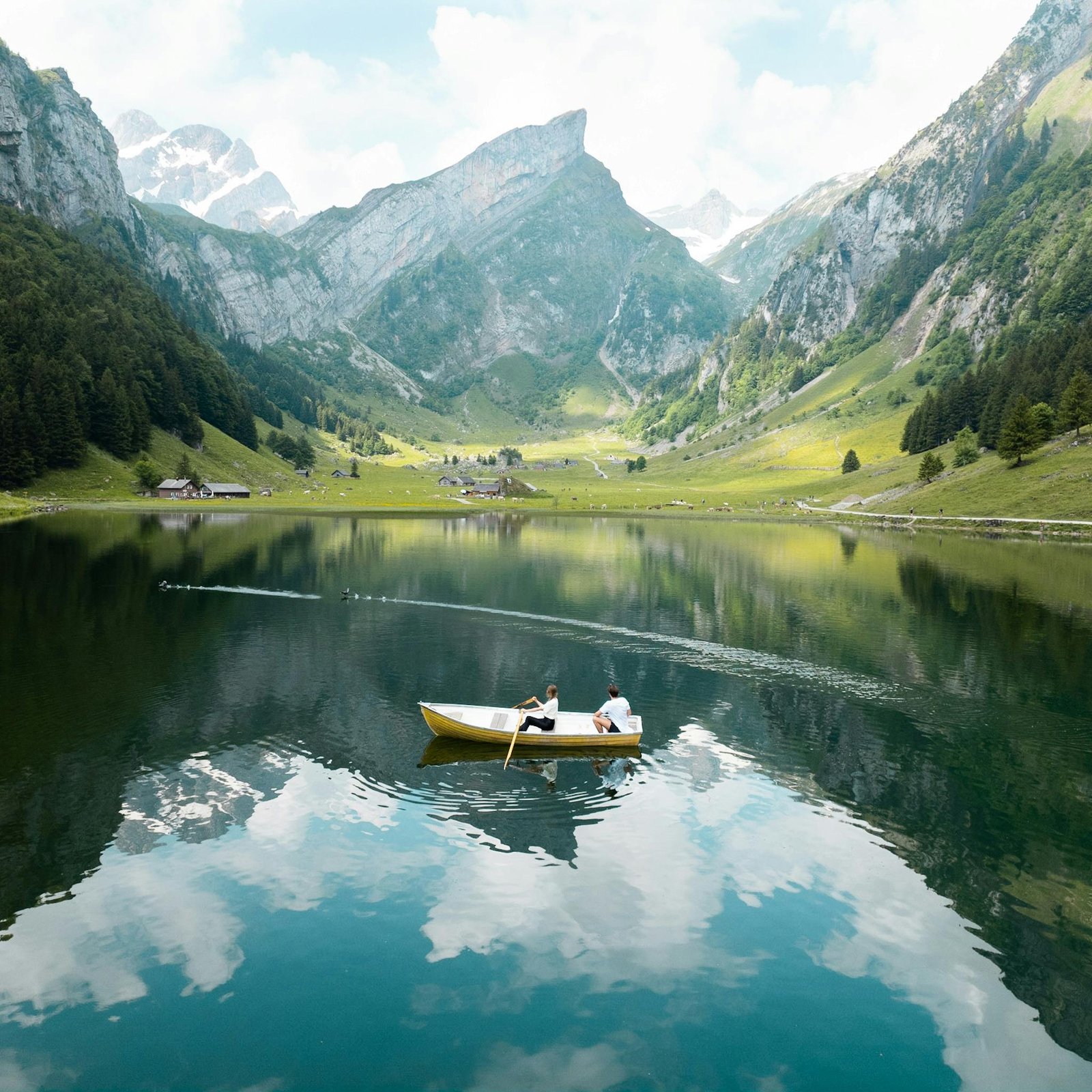 Two people enjoy a serene rowboat ride on a picturesque mountain lake. Switzerland. 