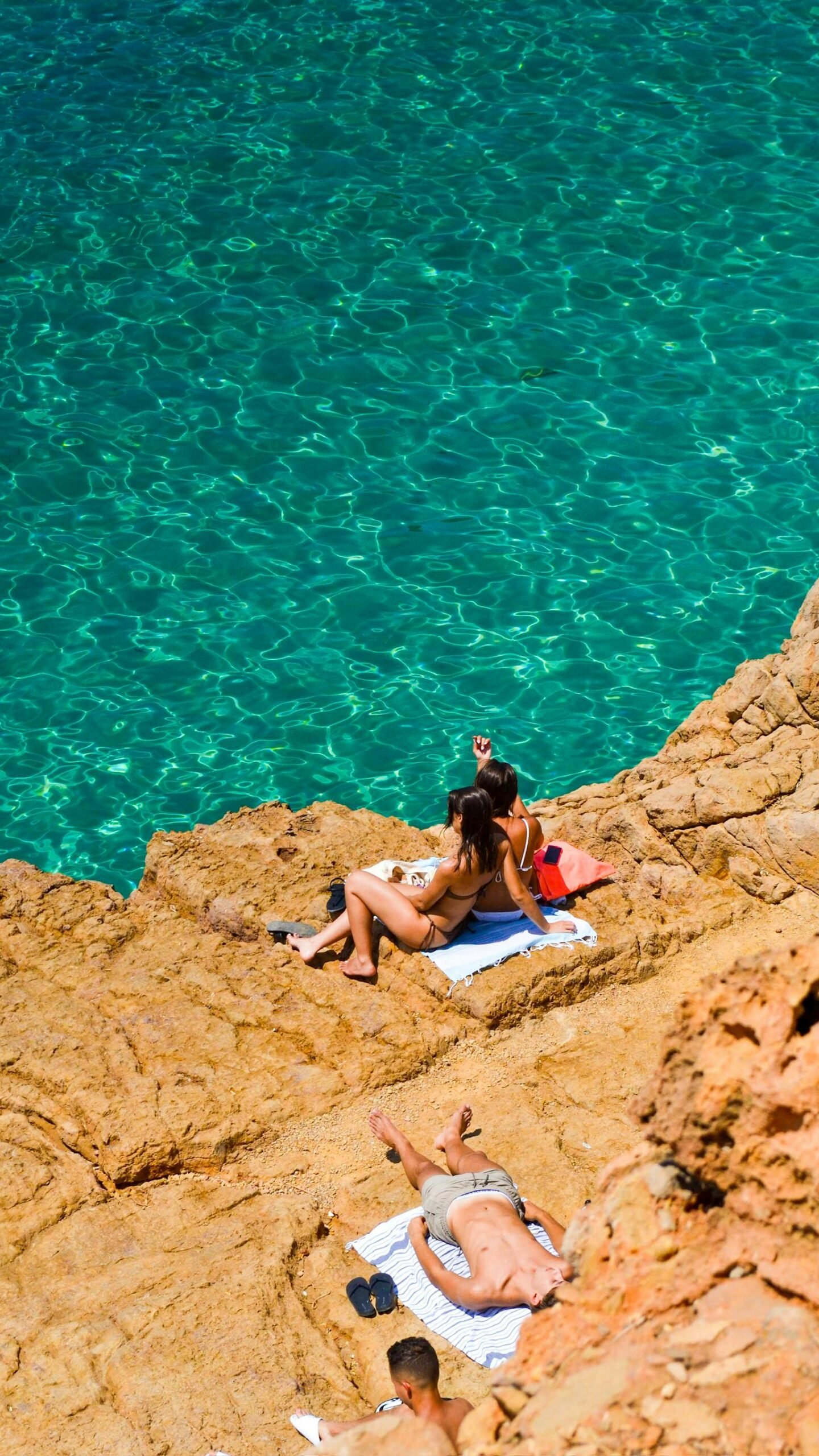 People sunbathing on rocky cliffs by a clear turquoise sea in Ibiza, perfect summer day.
